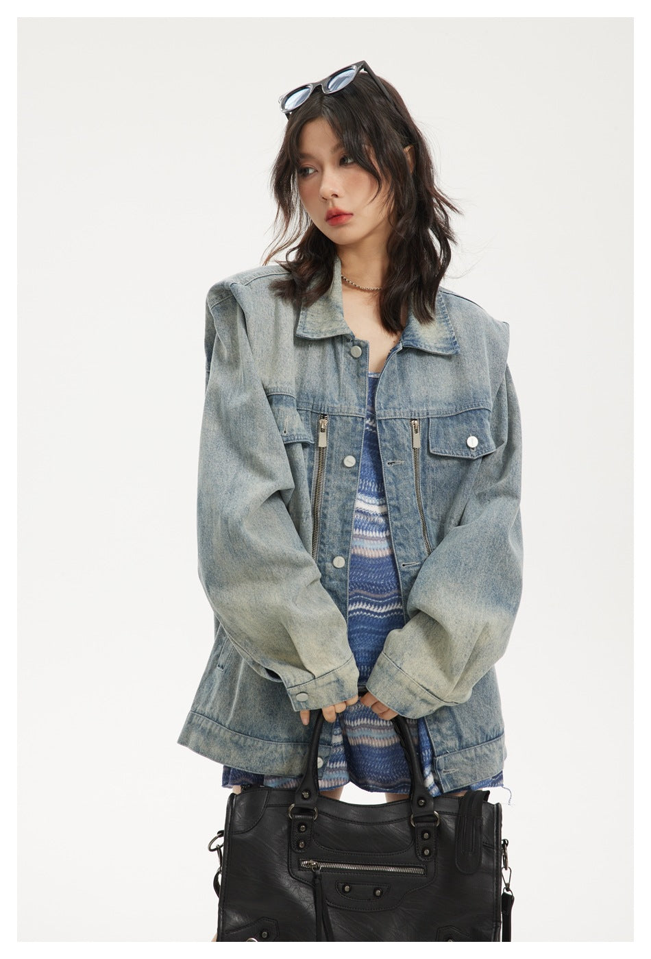Close-up of a model in an oversized washed denim jacket with zipper chest details, holding a black handbag