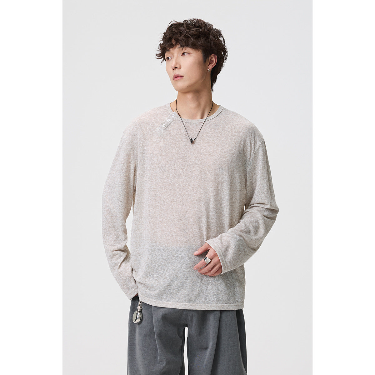 Model wearing a loose beige long-sleeve shirt with an asymmetrical button neckline, shown from the front.