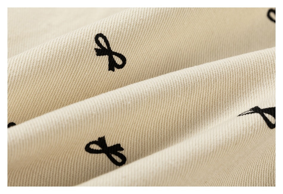 Macro view of beige fabric with black bow motifs, showing its diagonal woven texture.