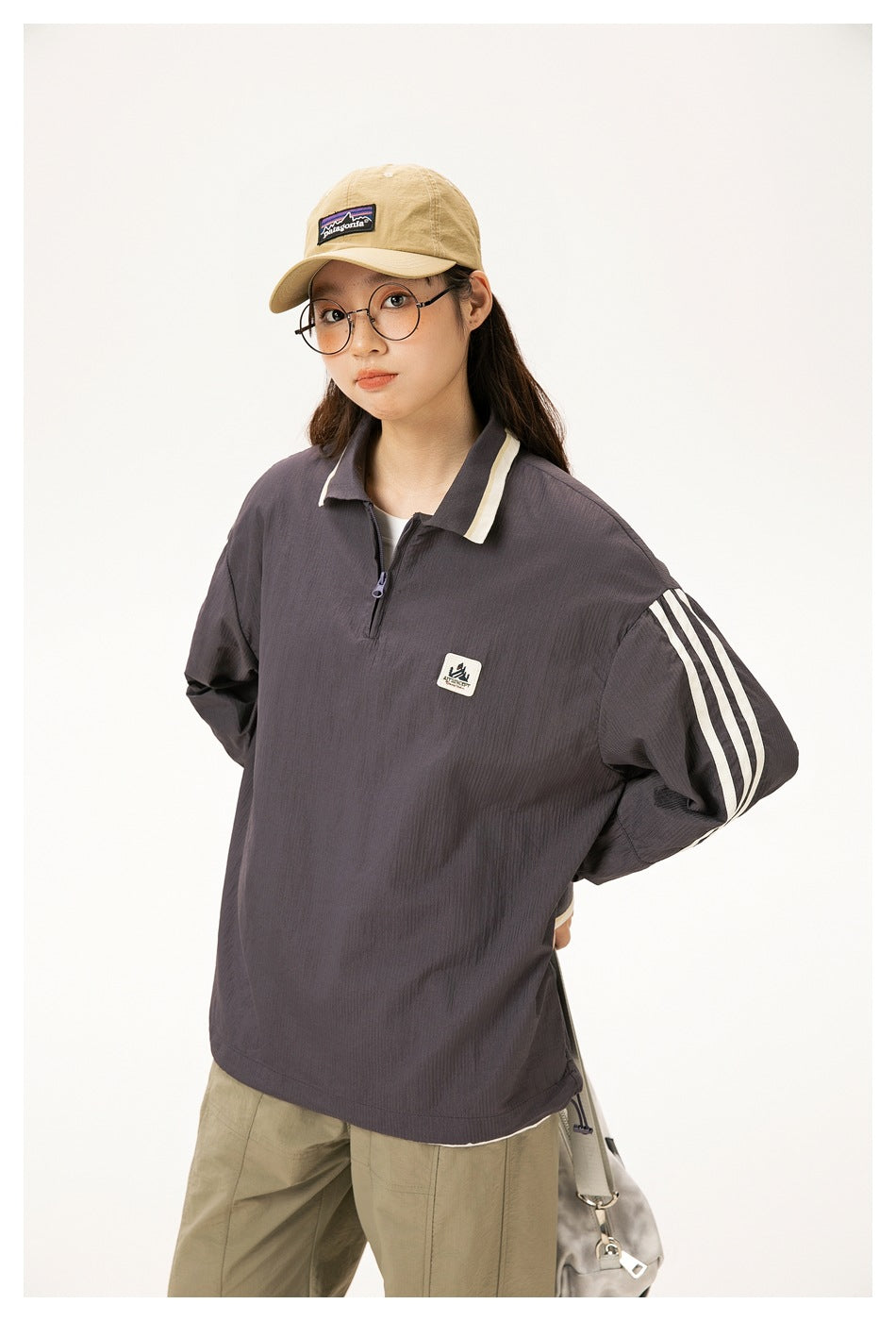 Model wearing a charcoal quarter-zip pullover with cream collar trim and sleeve stripes, paired with khaki trousers.