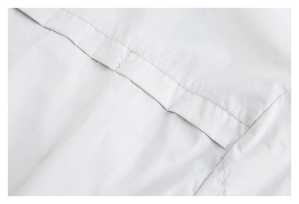 Close-up of white garment fabric with a folded edge and visible stitching.