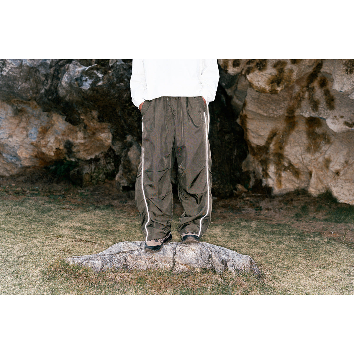 Person wearing charcoal loose-fit pants with white side piping outdoors; upper body is cropped out.