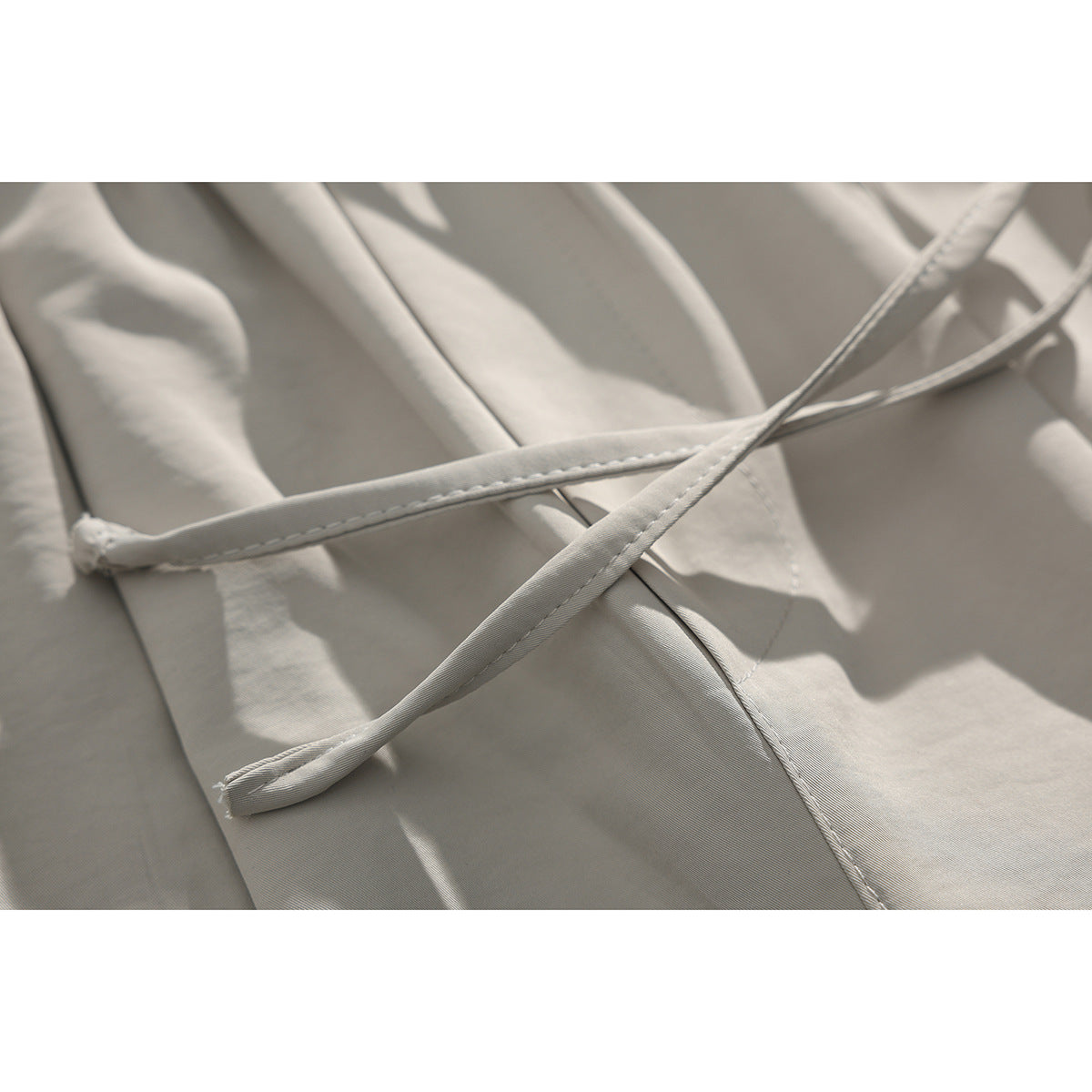 Close-up of light beige shorts with crossed drawstrings and visible stitching on the fabric.