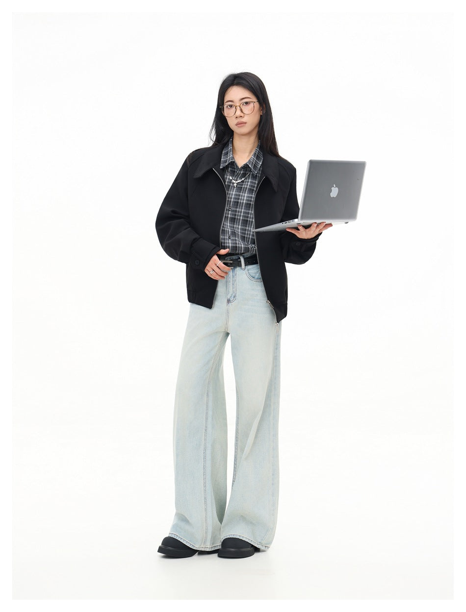 Model in black zip jacket, plaid shirt and light wide-leg jeans, holding an open laptop, three-quarter pose