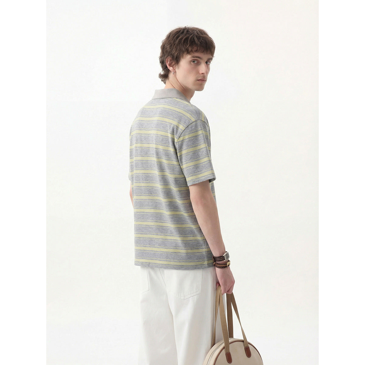 Model looking back while wearing a gray polo with pale yellow stripes and white trousers.