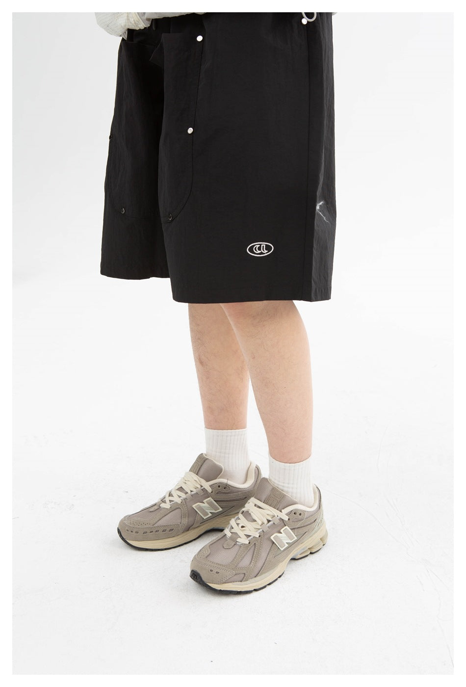 Cropped view of a person wearing black knee-length shorts with snap-fastened panels and a small white oval emblem.