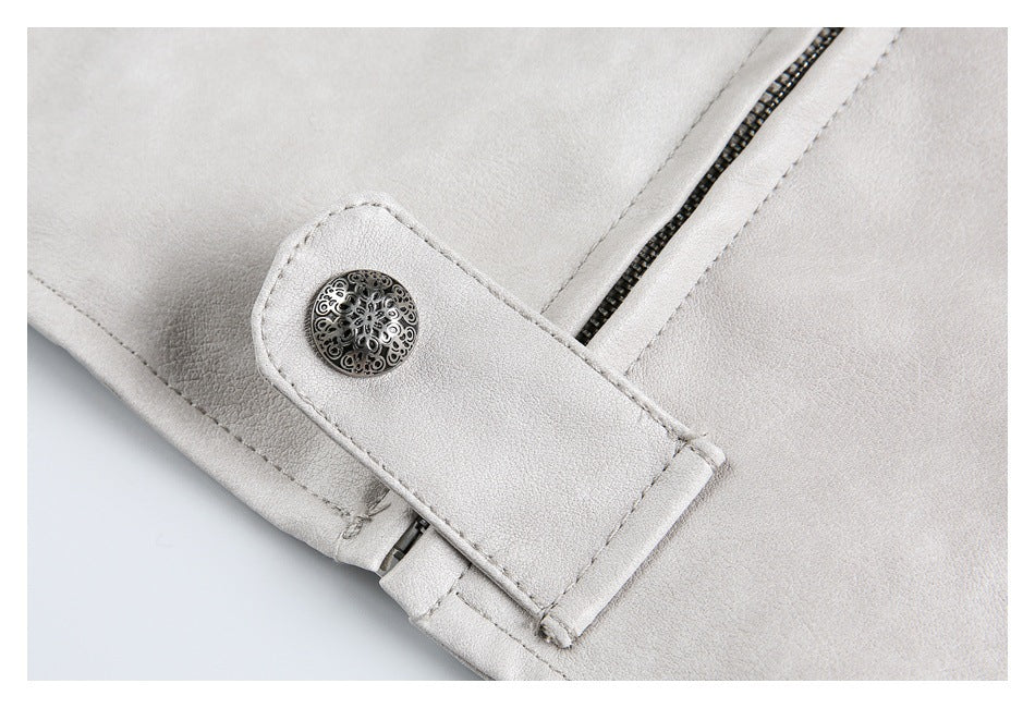 Close-up of a pale gray-beige garment with a diagonal zipper and ornate round snap on a tab.