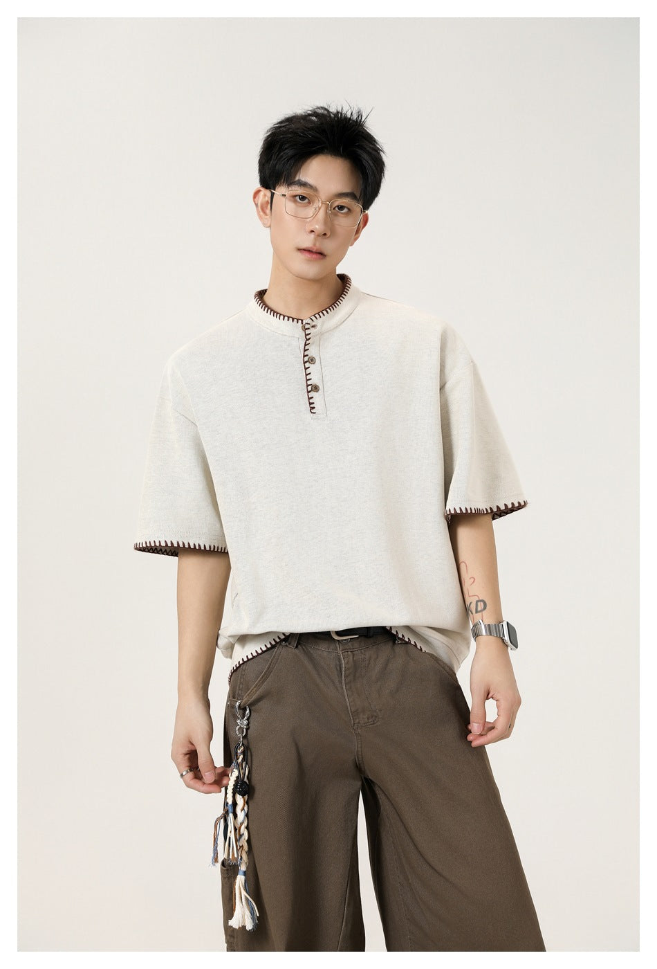 Front view of a model in an ivory short-sleeve henley with dark contrast stitching and brown trousers.