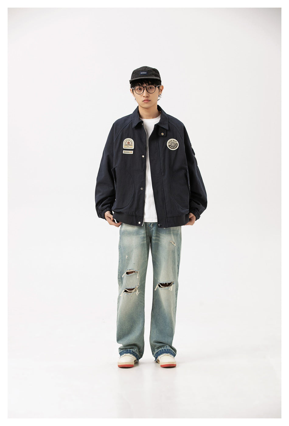 Model wearing navy patch-detail bomber jacket over a white tee with distressed light-wash jeans, full-length view