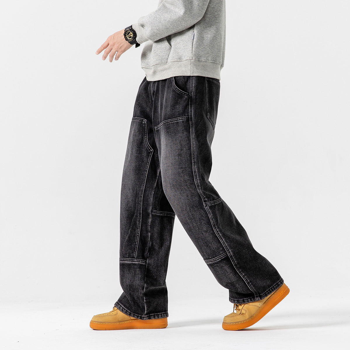 Model walking in loose black washed jeans with prominent contrast panel seams and a gray sweatshirt.