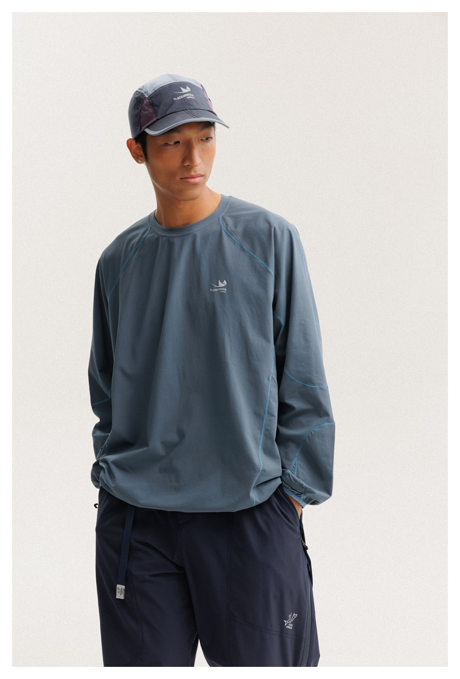 Closer view of a model wearing a blue-gray pullover with cyan seam details and navy pants.