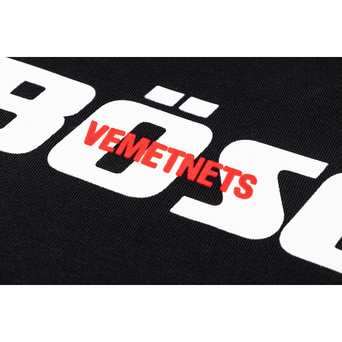 Close-up of a black T-shirt print with large white lettering and smaller red text.