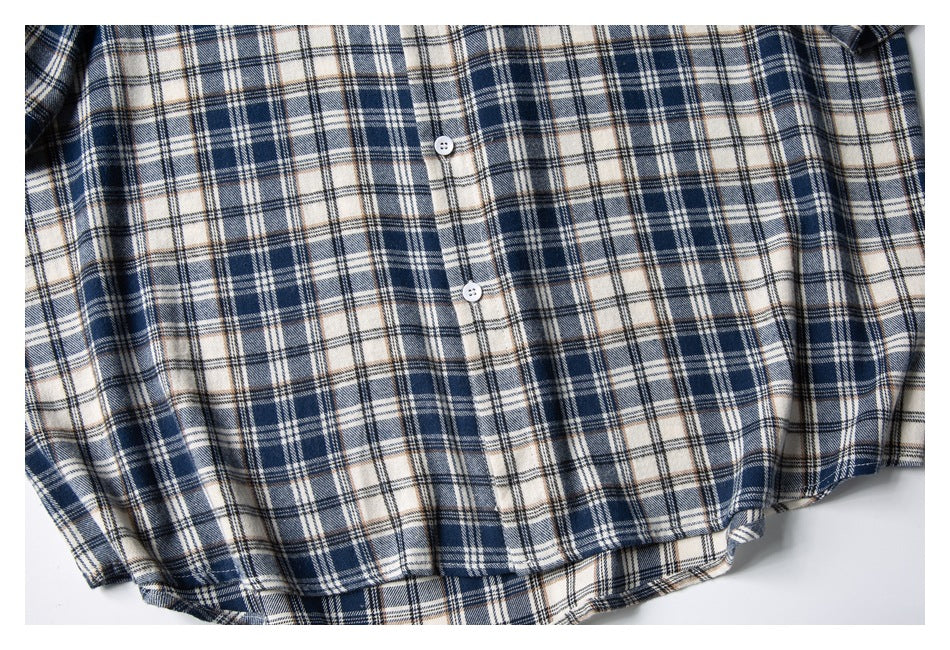 Flat-lay crop of the lower front of a navy, cream, and tan plaid button-up shirt.