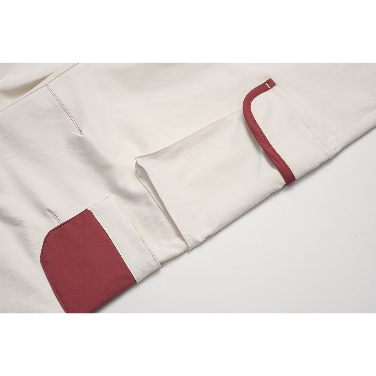 Close-up of cream cargo pants showing a red-trimmed flap pocket and red patch pocket.