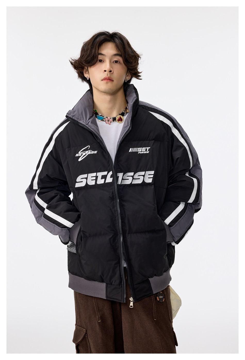Model wearing a zipped black quilted stand-collar jacket with gray sleeves, white stripes and chest lettering