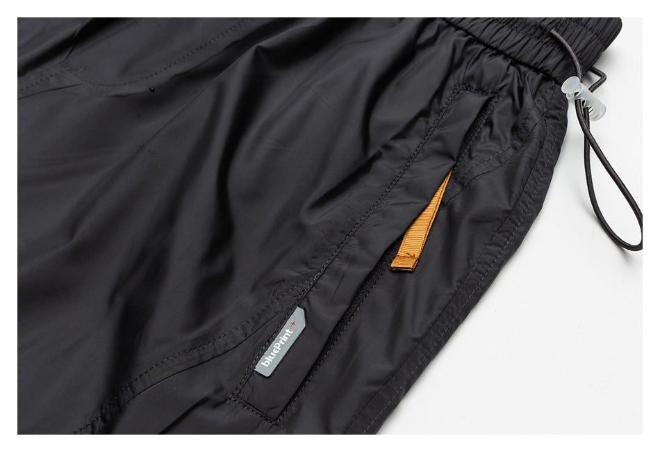 Close-up of black shorts with a zip pocket, orange pull tab, and small attached brand label.