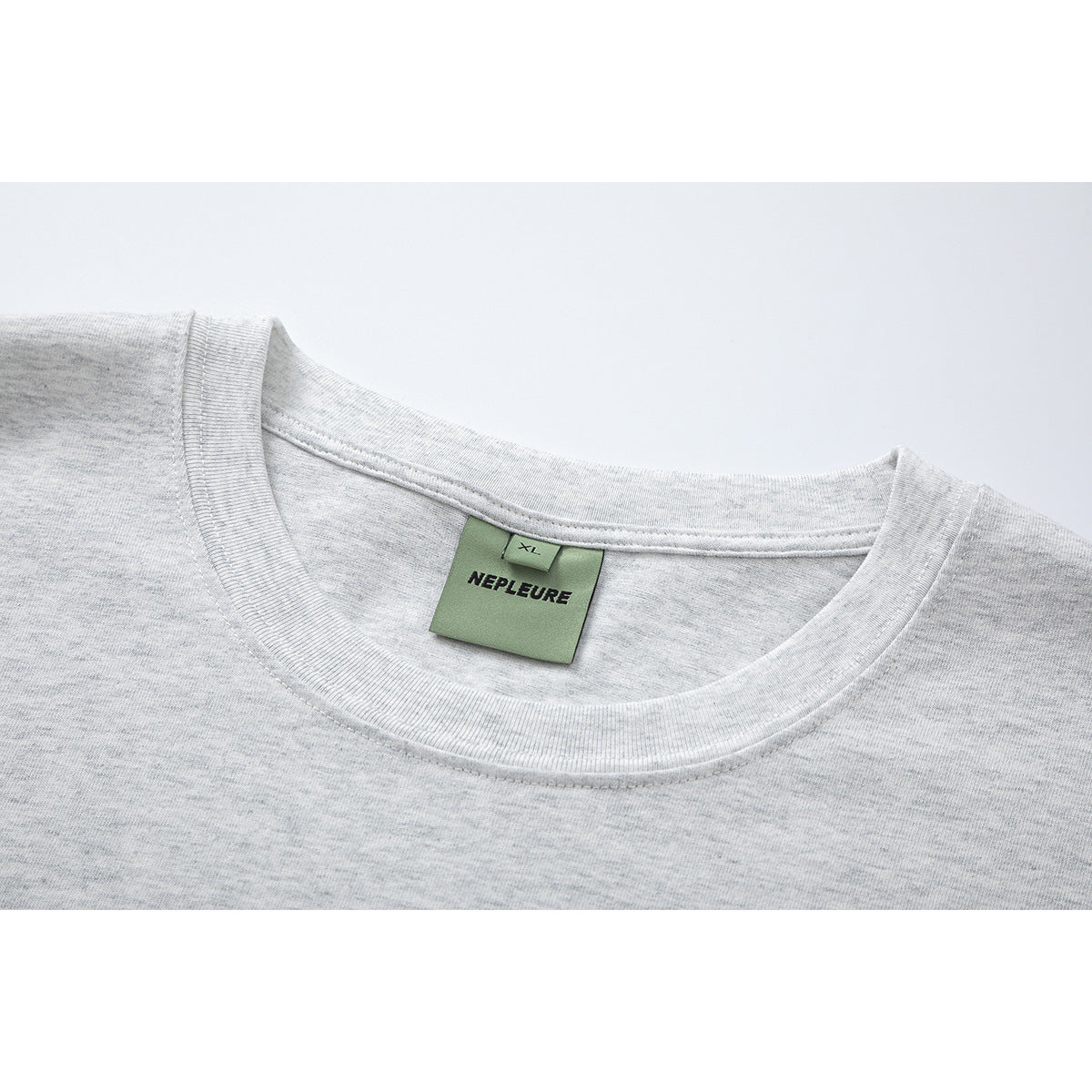 Close-up of a light heather gray T-shirt neckline with a green NEPLEURE label marked XL.