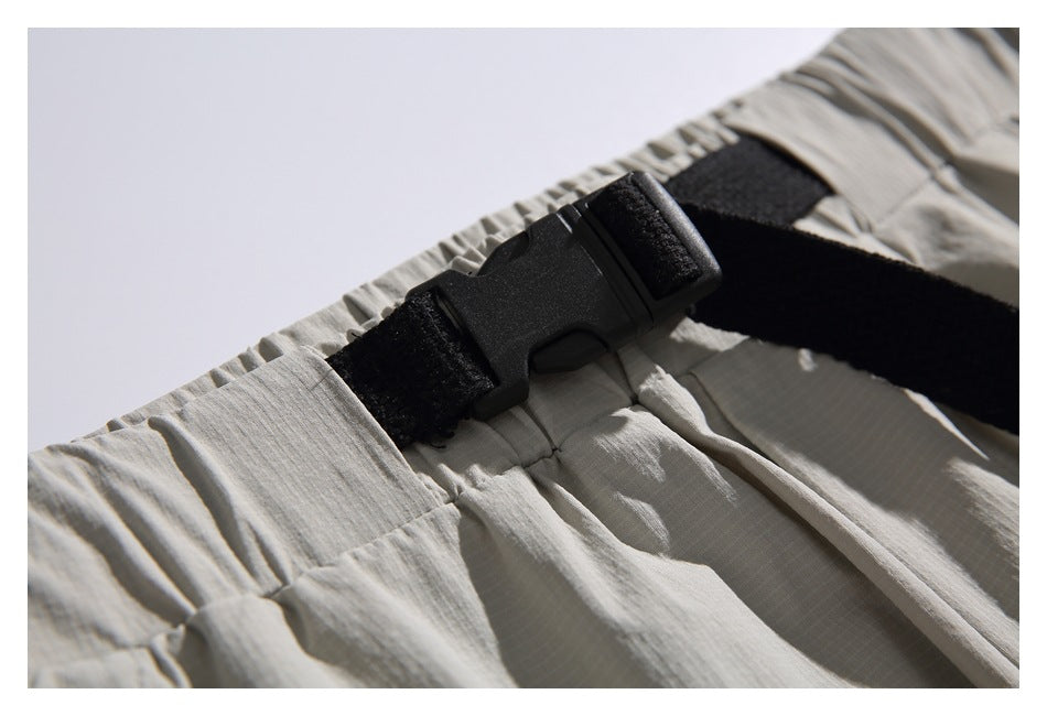 Close-up of light gray-beige trousers with an elastic waistband and black adjustable buckle strap.