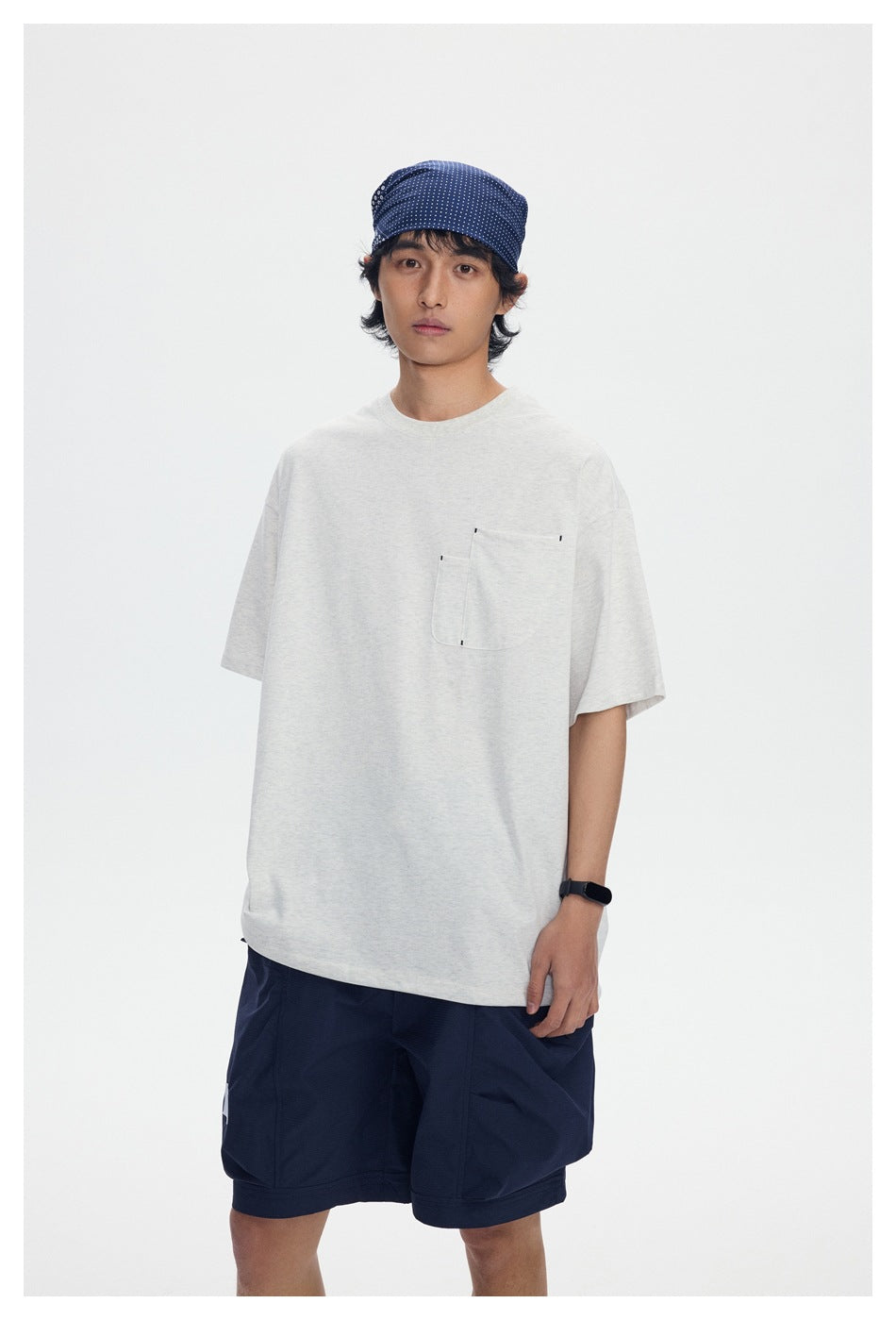 Model wearing a light gray short-sleeve pocket T-shirt and navy shorts, shown from the front.