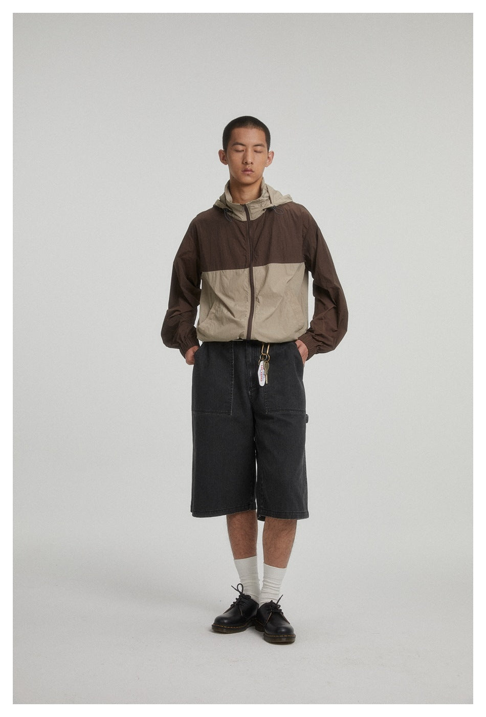 Model facing forward in a brown and beige hooded color-block jacket and black knee-length shorts.