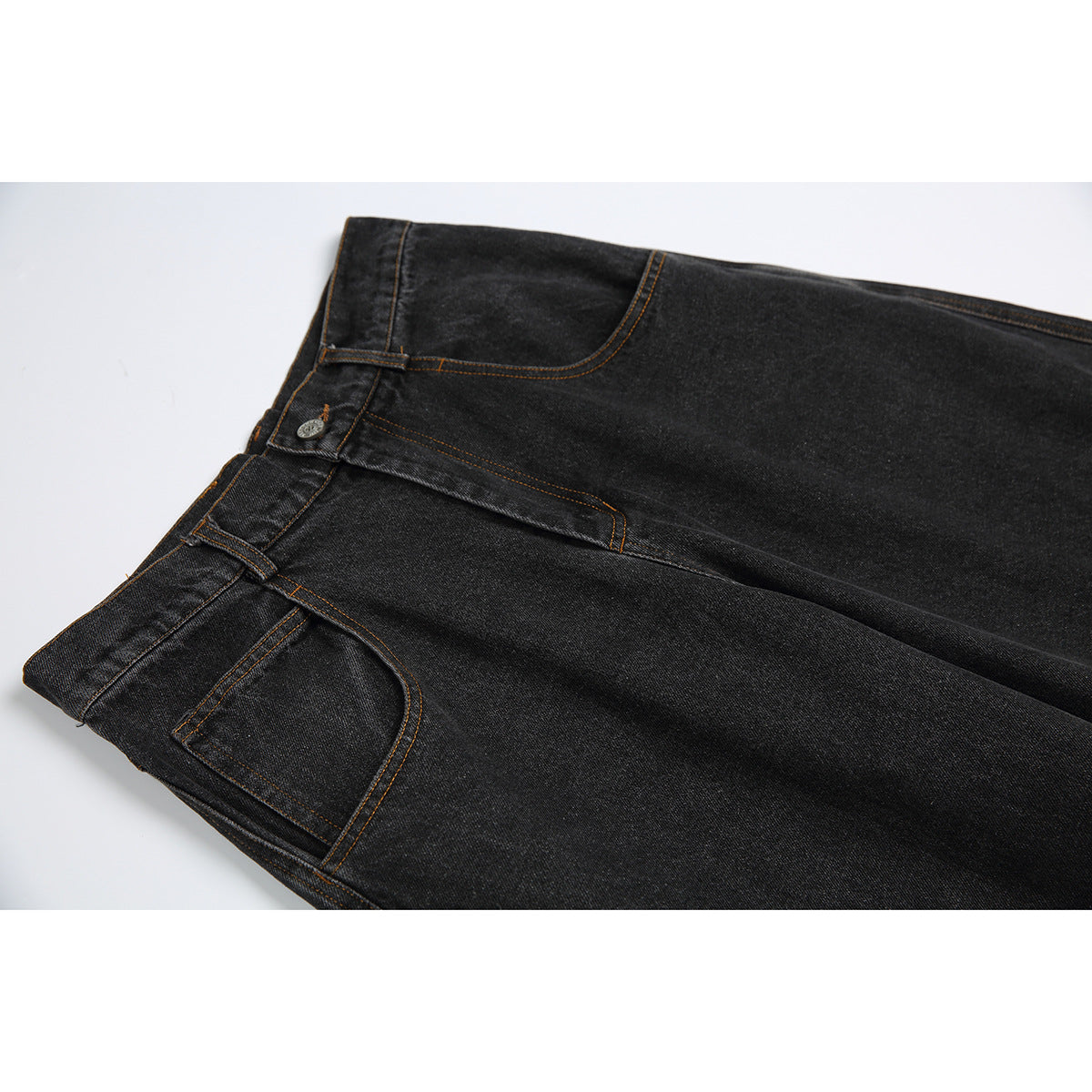 Close-up of black denim jeans showing the waistband, button, front pocket, and orange-brown stitching.