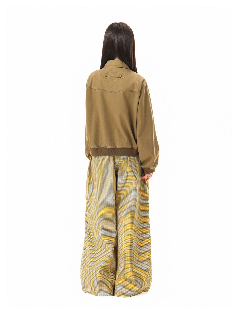 Rear view of a model wearing a tan jacket with ribbed hem and cuffs, paired with yellow plaid wide-leg trousers.