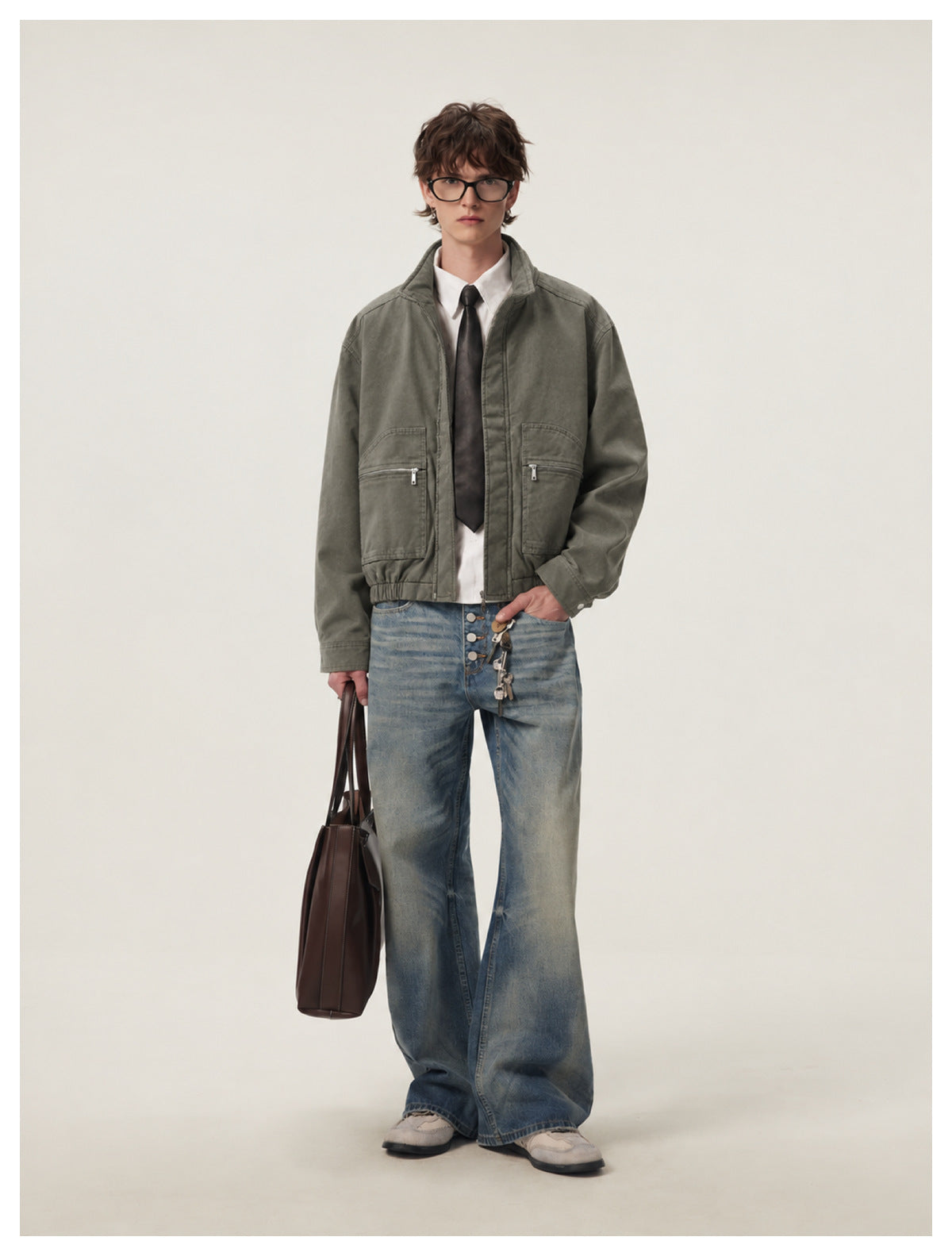 Model wearing army green cropped jacket zipped over a white shirt and tie with wide-leg jeans and a brown tote