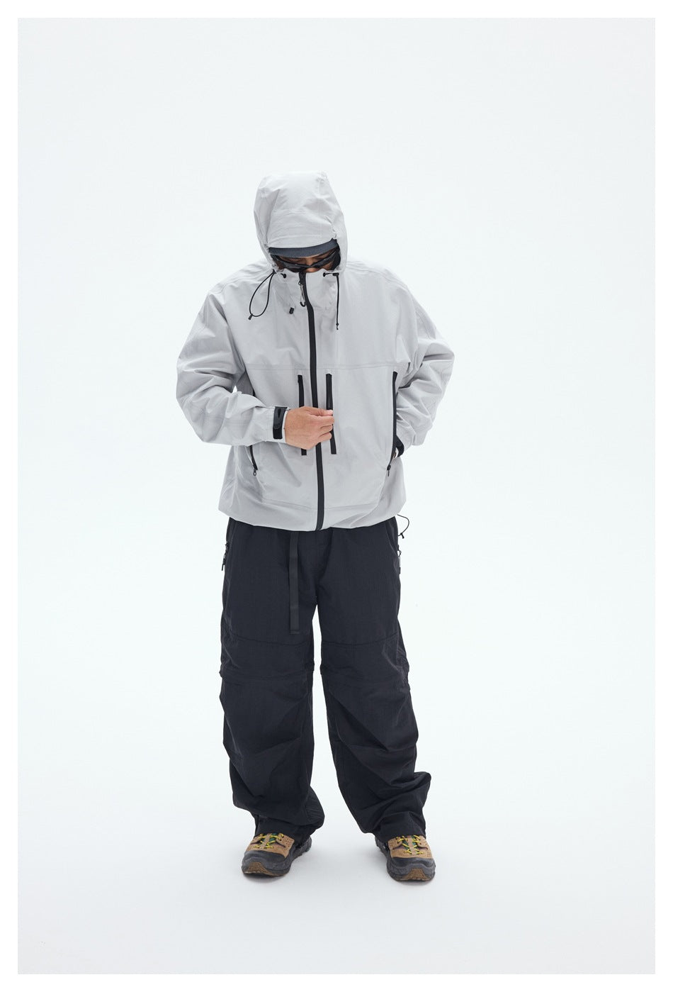 Model wearing a light gray hooded jacket with black zippers and loose black pants, standing against a white background.