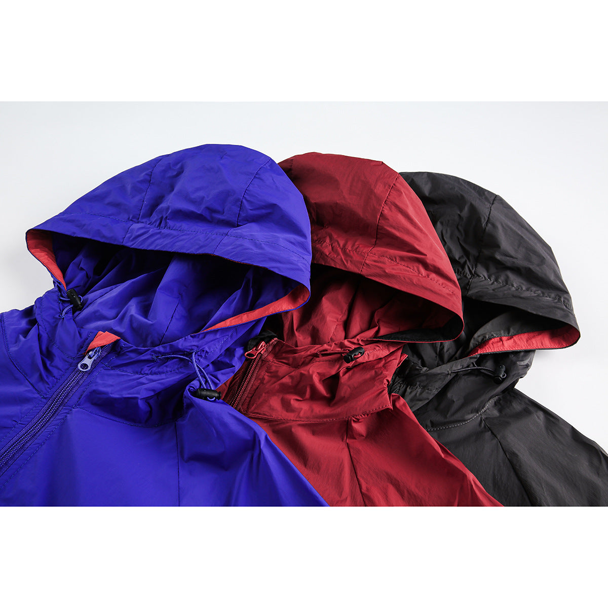 Close-up of three hooded jackets in blue, red, and black, showing lined hoods and front zippers.