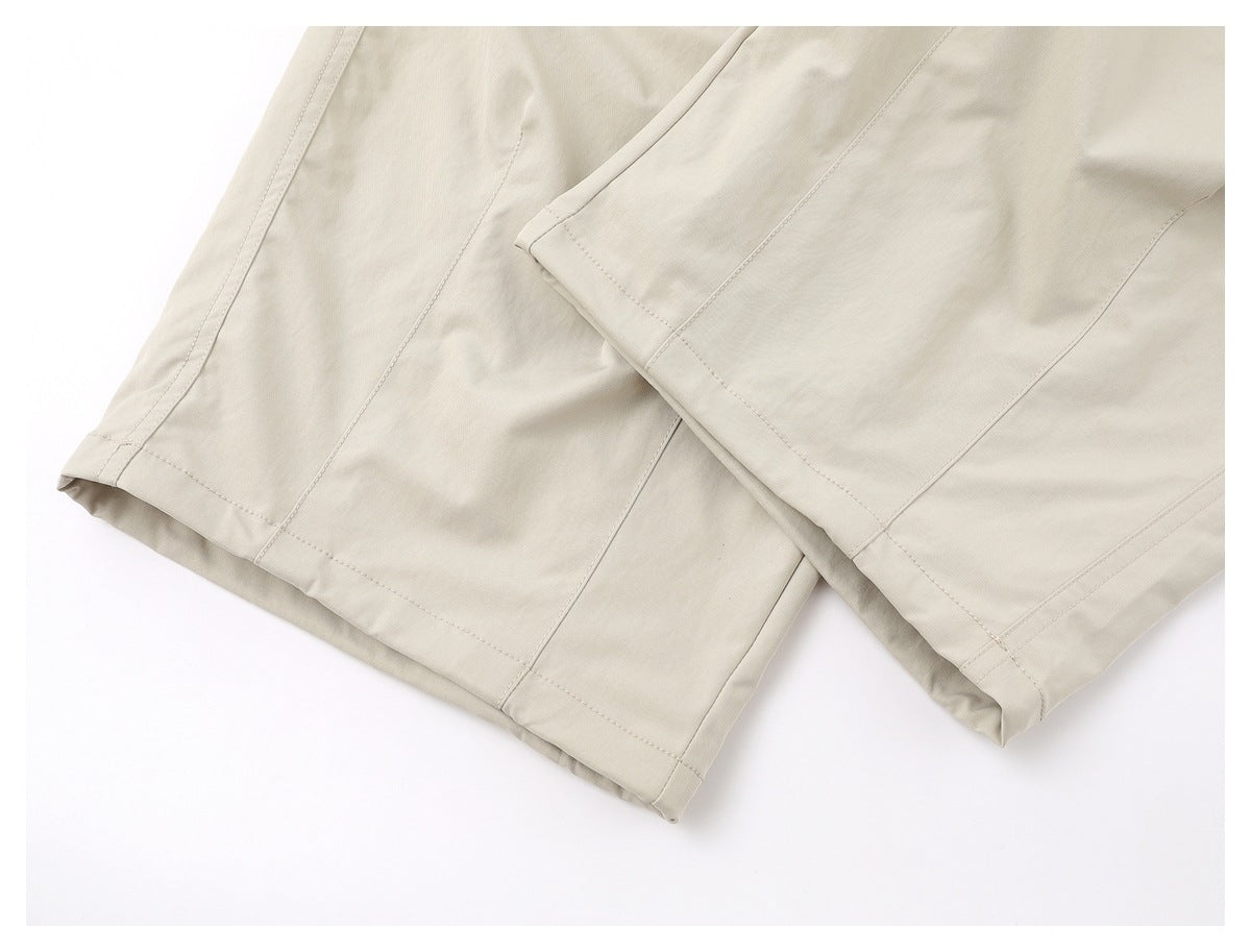 Close-up of beige shorts showing overlapping leg hems and stitched panel seams.