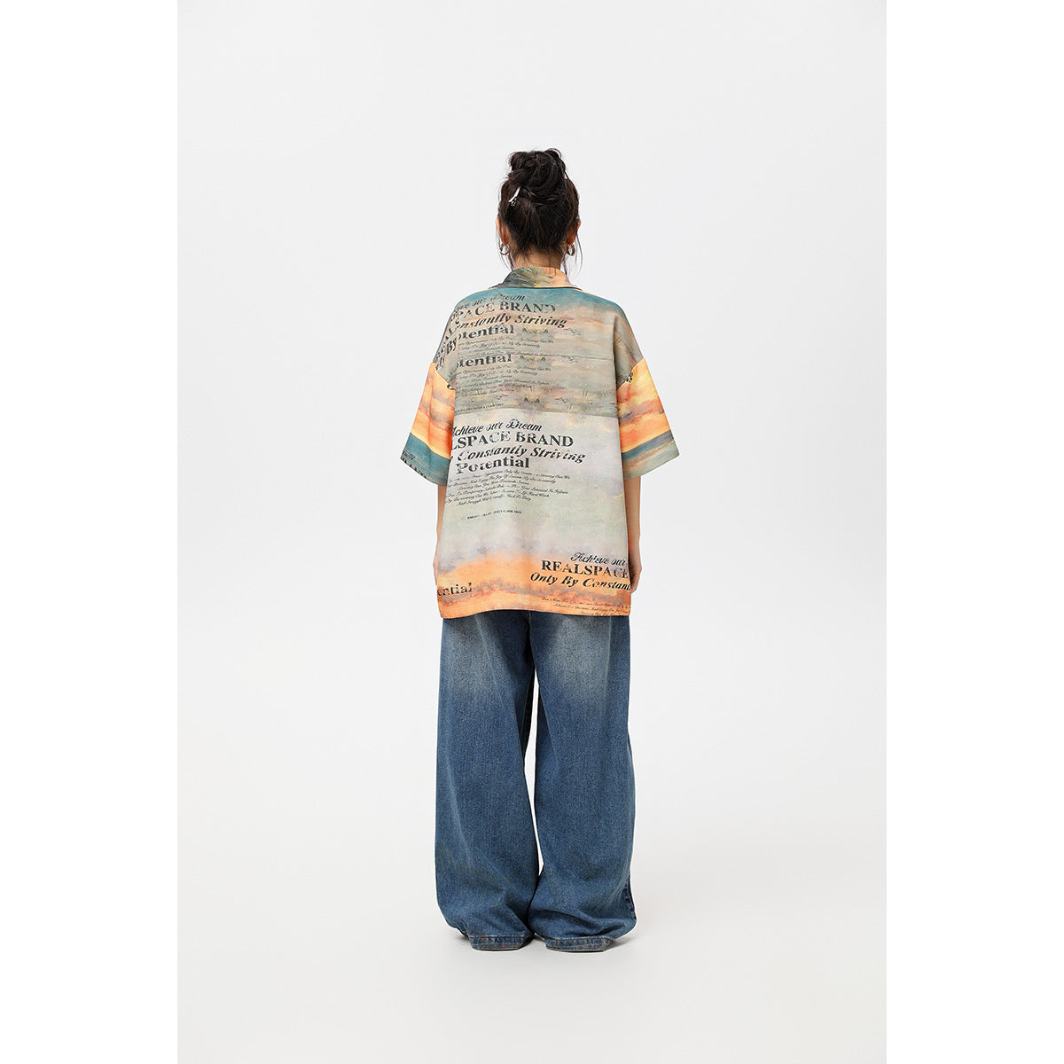 Back view of a model wearing a multicolored text-print short-sleeve shirt and wide-leg blue jeans.