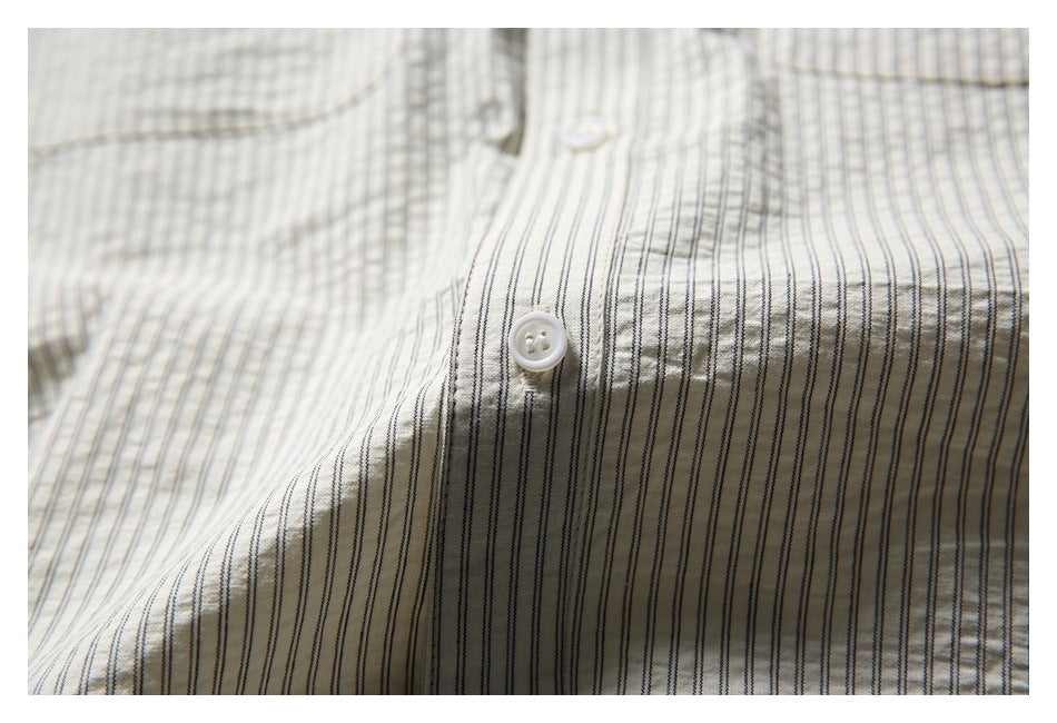 Detail of a white button and fine dark stripes on the cream shirt fabric.