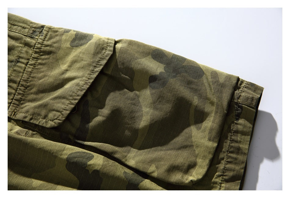 Close-up of a large flap cargo pocket and stitched hem on olive camouflage shorts.