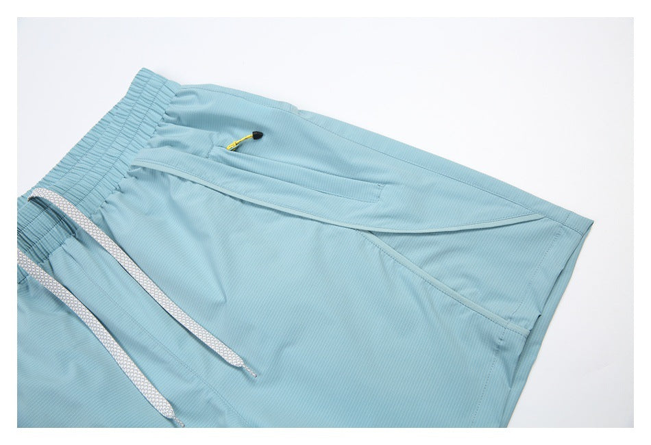Close-up of pale blue shorts showing a side zip pocket, yellow pull, and curved panel seams.