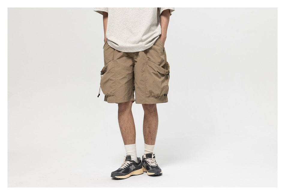 Model wearing khaki cargo shorts with a gray tee, cream socks and sneakers, cropped from chest down, front view