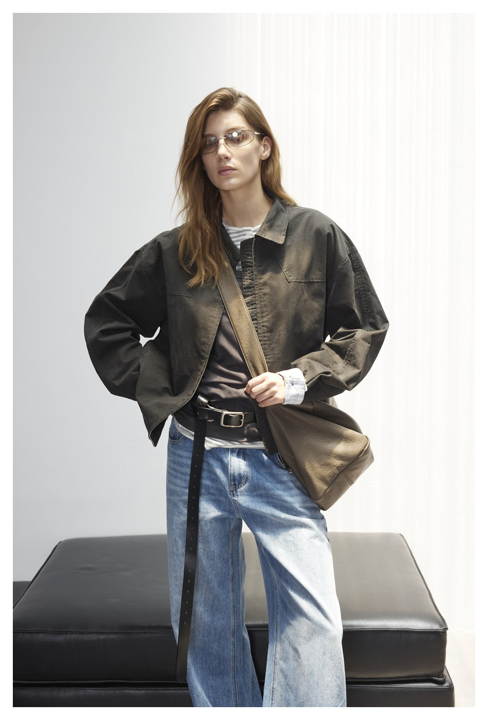 Front view of a model wearing a dark olive oversized jacket with chest pockets, layered tops, and wide-leg blue jeans.