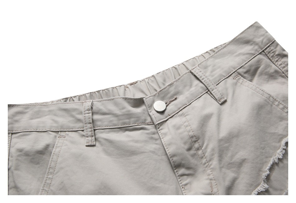 Close-up of light gray shorts' waistband, metal button, belt loops, and front pocket edge.