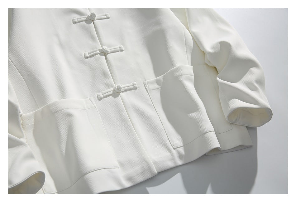 Cropped front view of a white jacket with knotted frog closures, long sleeves and large patch pockets.