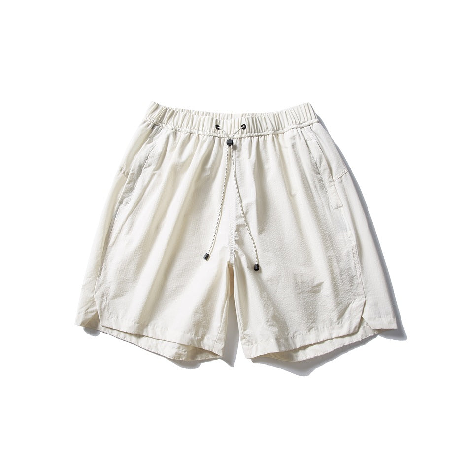 Cream white drawstring shorts with elastic waistband, side pockets and curved side-slit hems, flat lay