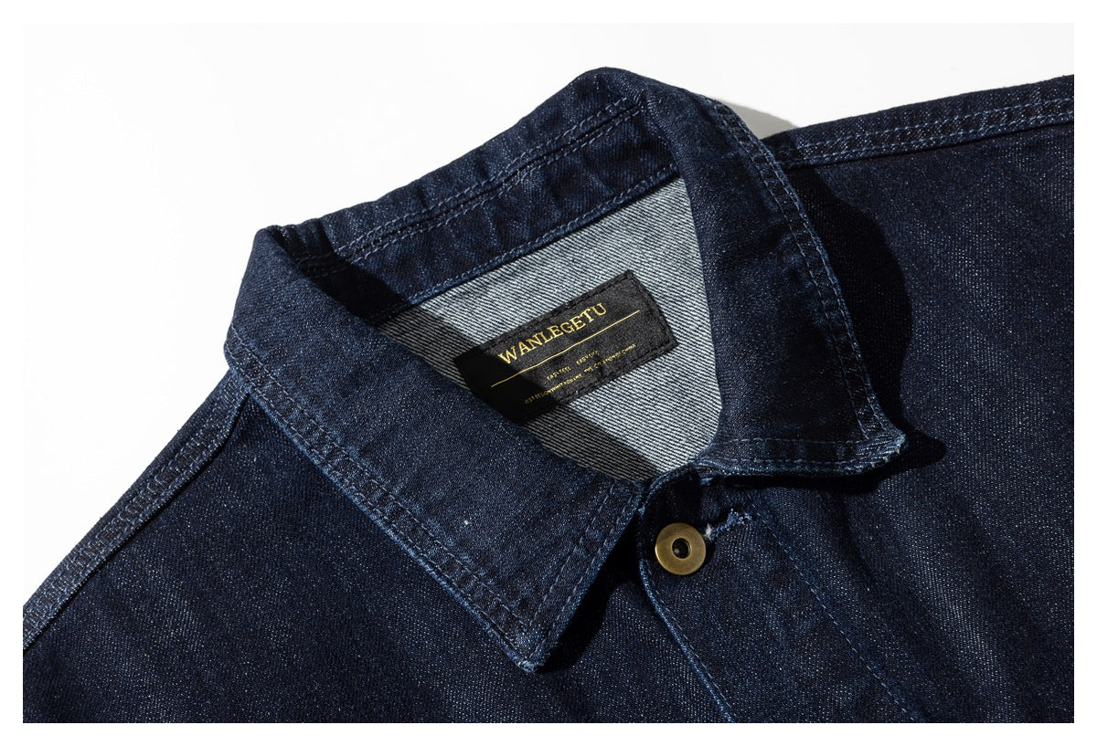 Close-up of a dark indigo denim jacket collar, showing a black-and-gold sewn label and brass button.