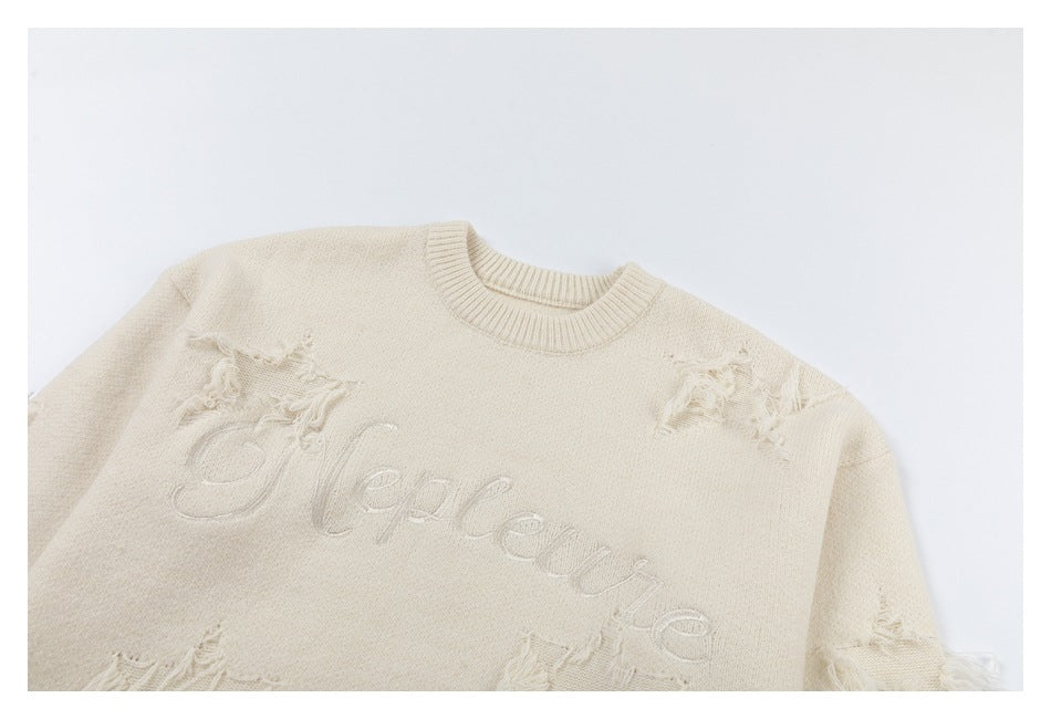 Cropped view of an ivory sweater front with raised script embroidery and distressed patches near the shoulders.