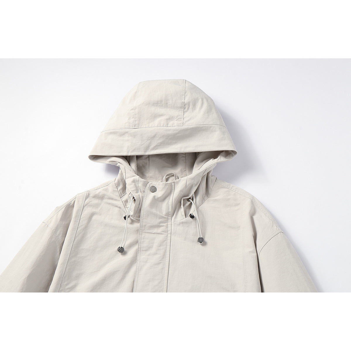 Close-up of an off-white hooded jacket with drawcords, metal toggles, and a snap-button storm flap.