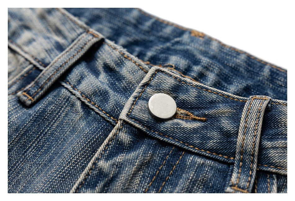 Close-up of the metal button, belt loop and stitched waistband on faded blue jeans.