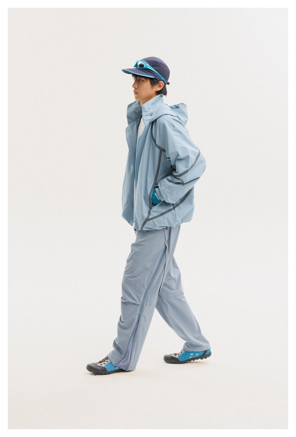 Model walking in a pale blue hooded jacket with dark trim and matching pants, shown from the side.