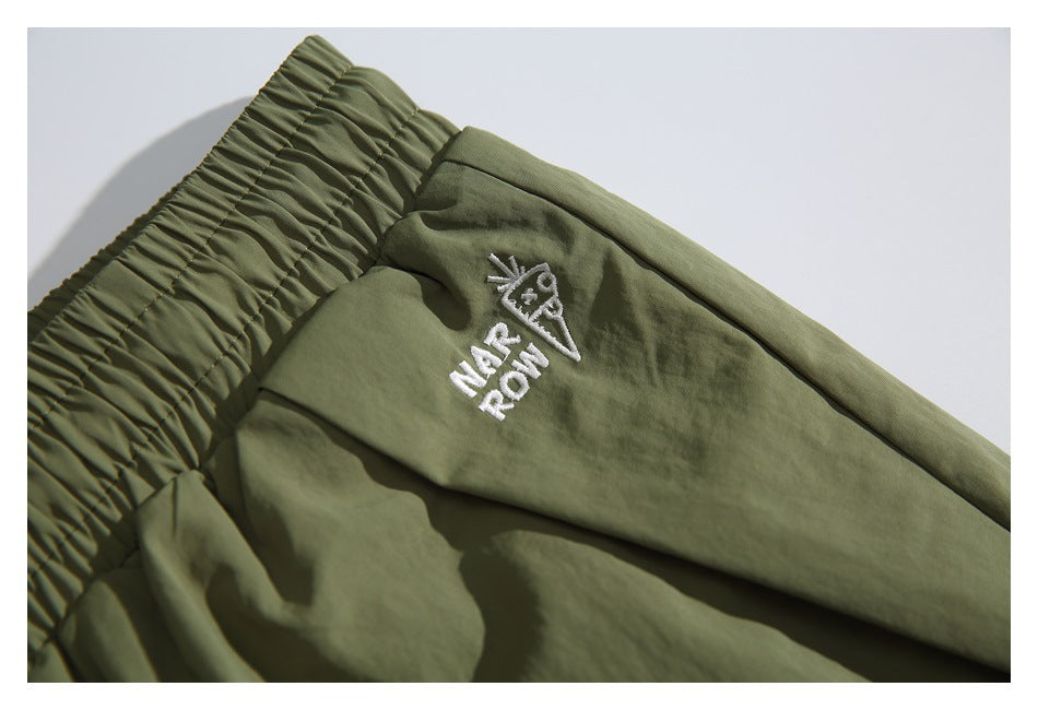 Olive-green pants detail showing a gathered waistband and white embroidered carrot graphic with “MR TOWN” text.