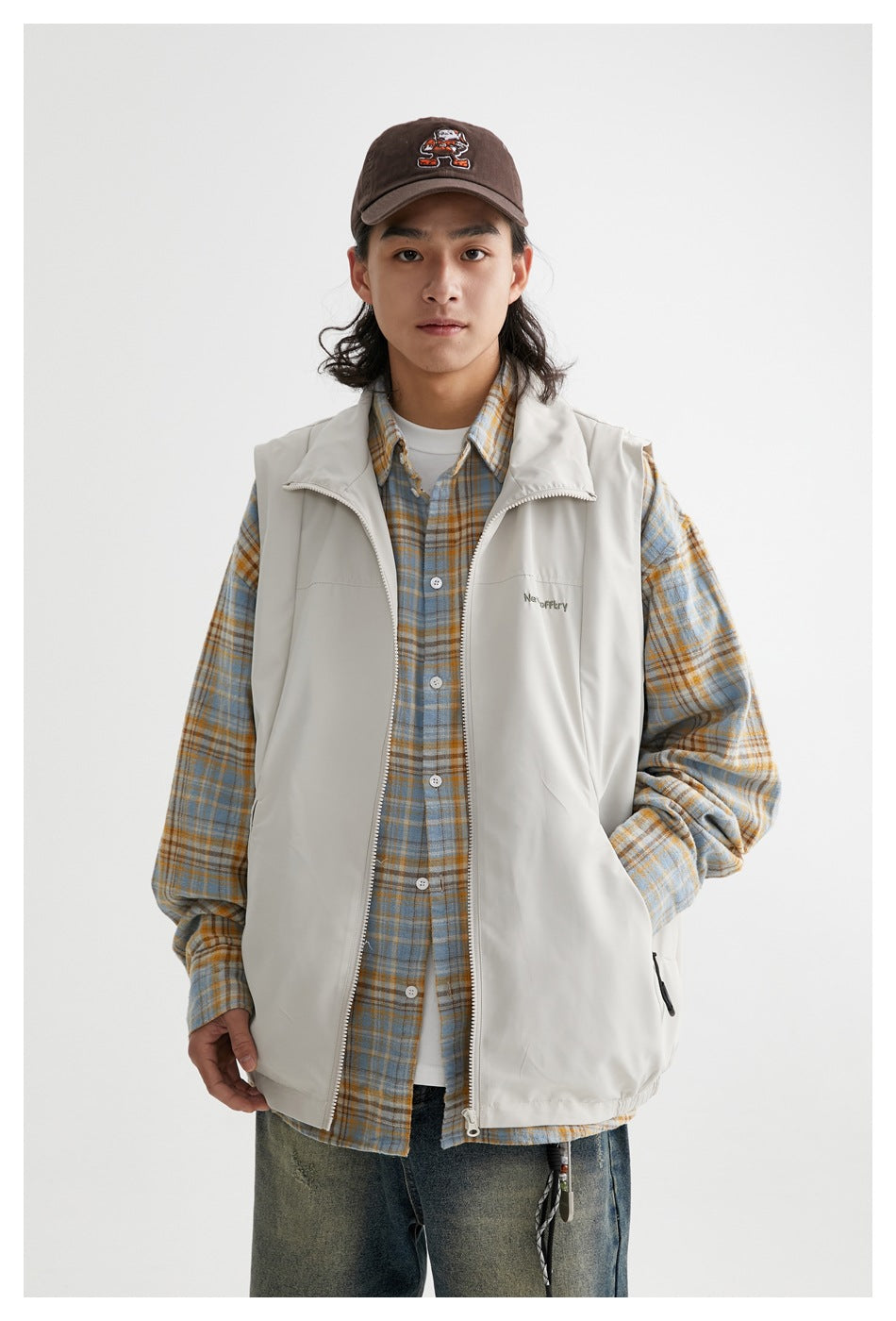 Front view of a model wearing a light gray zip-front vest over a blue and tan plaid shirt.