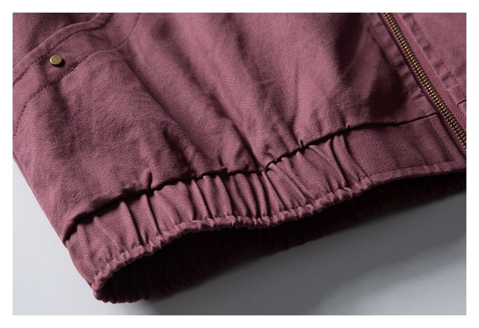 Close-up of a mauve jacket's gathered elastic hem, brass rivet, and zipper.
