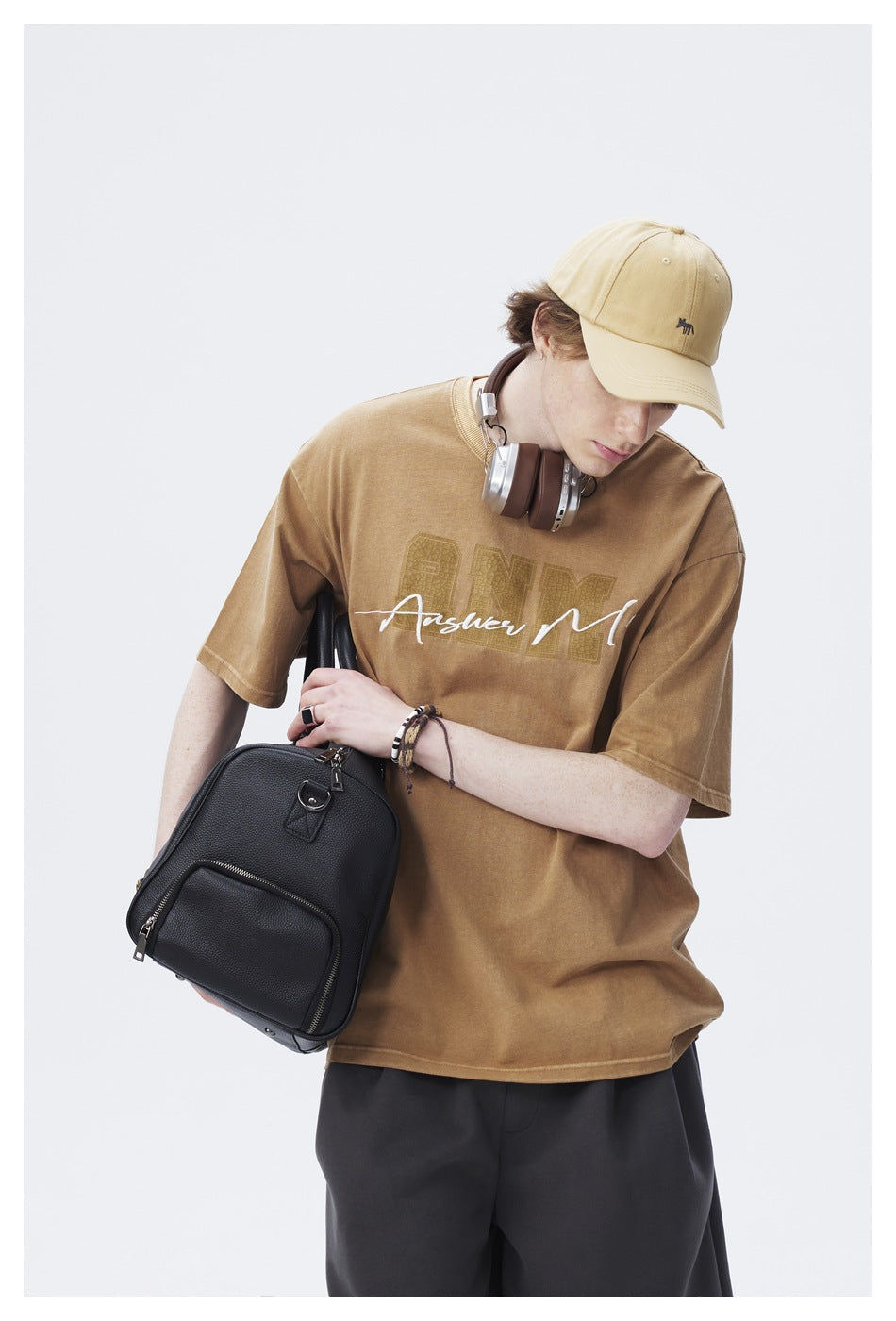 Close view of a model wearing a tan graphic T-shirt, with a beige cap and charcoal shorts.
