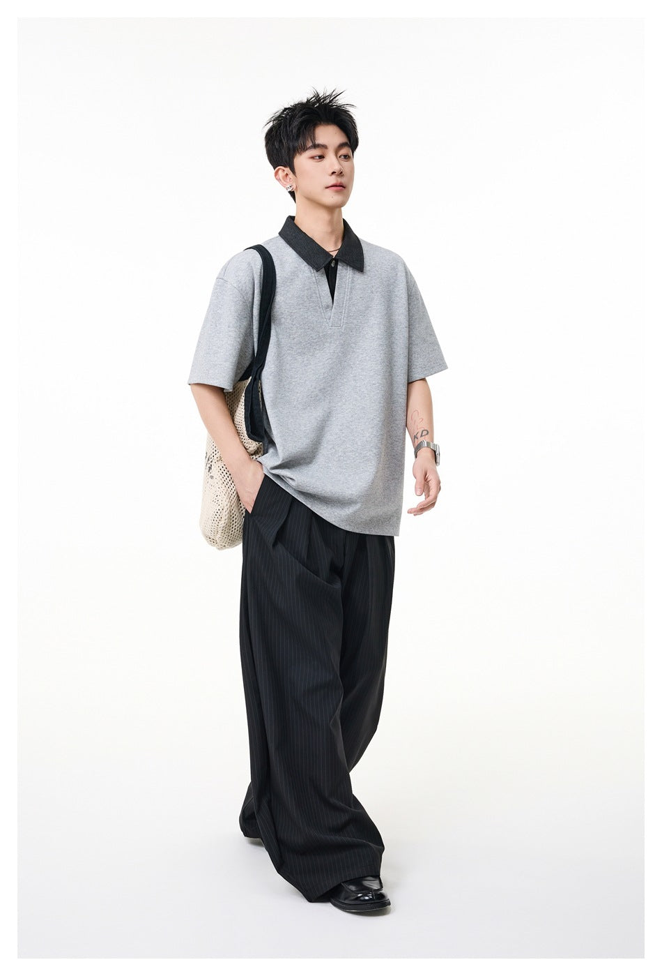 Model wearing a gray short-sleeve polo with a contrasting dark collar and loose black pinstripe trousers.