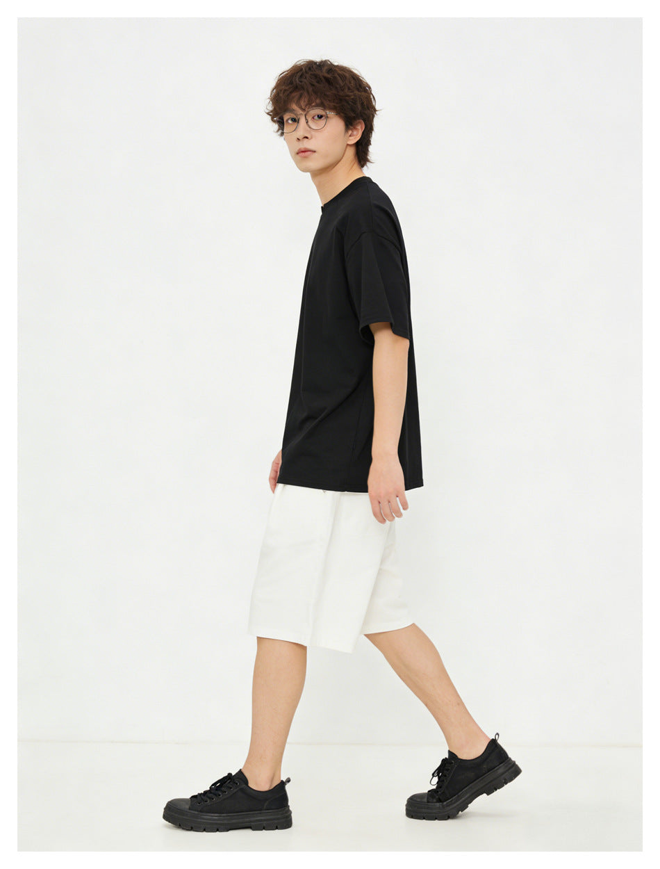 Model wearing a loose black short-sleeve crew-neck T-shirt and white shorts, shown in side view.